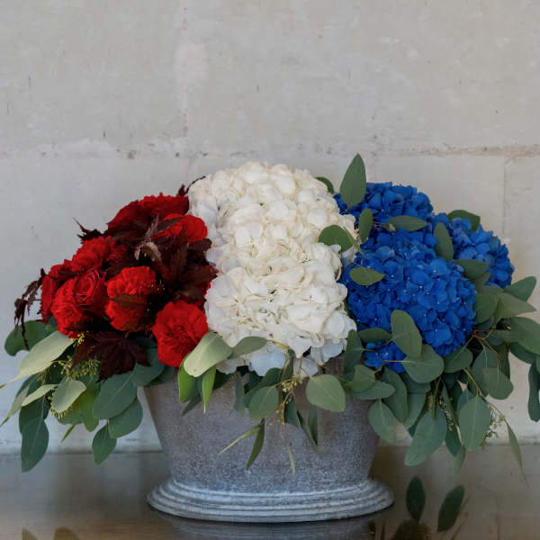 Red, white, and blue flowers arranged in a gray metal container