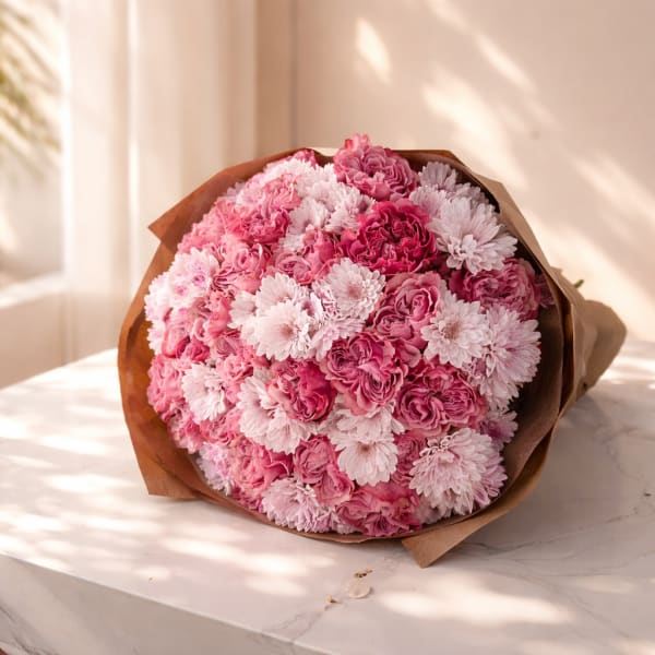 Round bouquet of pink and white flowers wrapped in brown paper on a marble surface