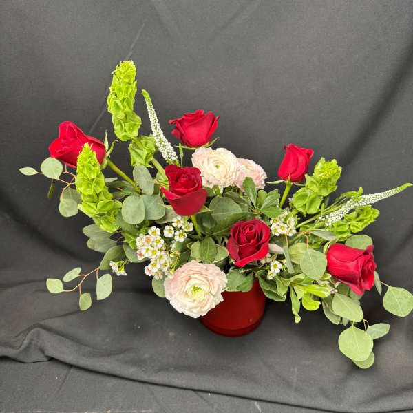 Red roses and pale ranunculus arranged in a red vase