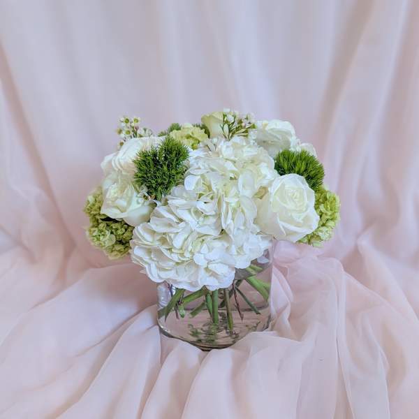 White floral bouquet in a clear glass vase with pale pink draping