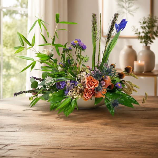 Low floral arrangement with orange roses and purple blooms in a shallow bowl
