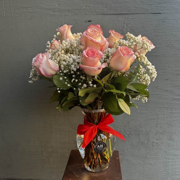 Pink roses in a clear glass vase with baby's breath and a red ribbon