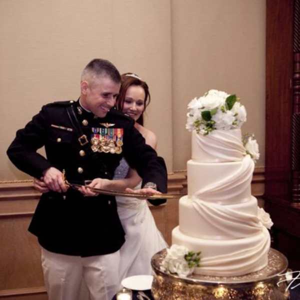 Bride and groom cutting a tall white wedding cake with white flowers