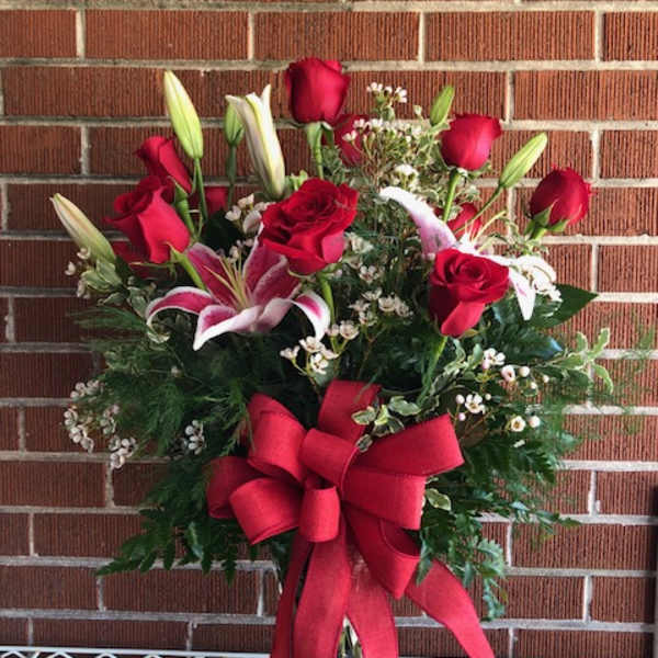 Red roses and lilies in a glass vase with a large red bow