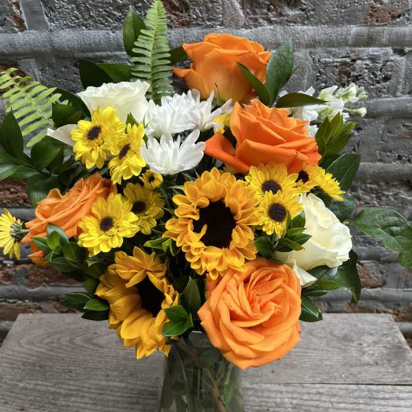 Orange roses and yellow sunflowers in a glass vase