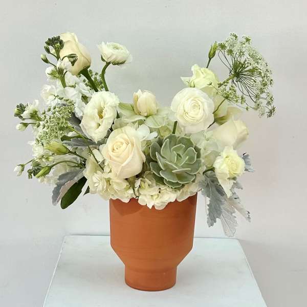 White floral arrangement in a terracotta vase with a green succulent