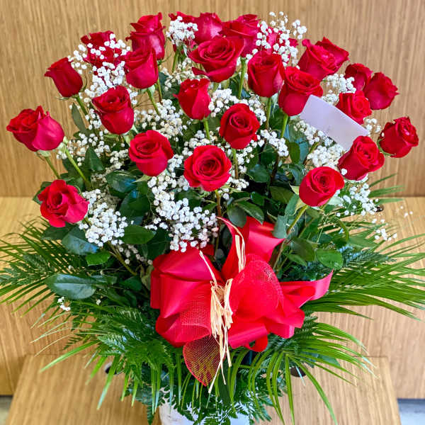 Red roses arranged in a white basket with baby's breath and a red bow
