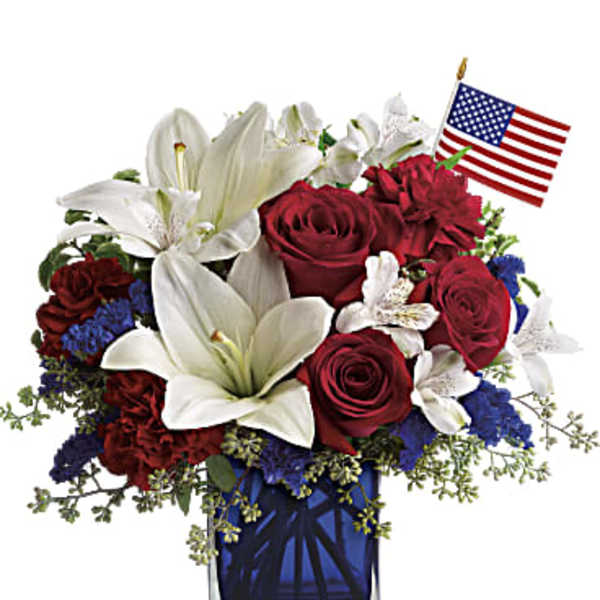 Red roses and white lilies in a blue glass vase with a small American flag