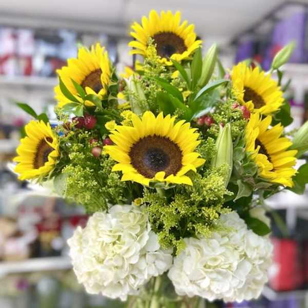 Tall arrangement of yellow sunflowers and white hydrangeas in a clear glass vase