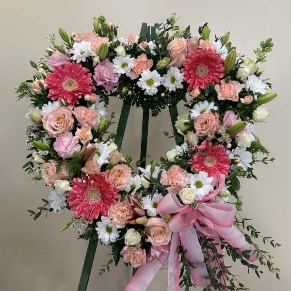 Heart-shaped floral wreath on a stand with pink and white flowers and a pink ribbon