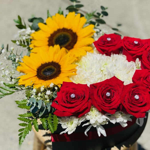 Bouquet of red roses, sunflowers, and white flowers in a black box