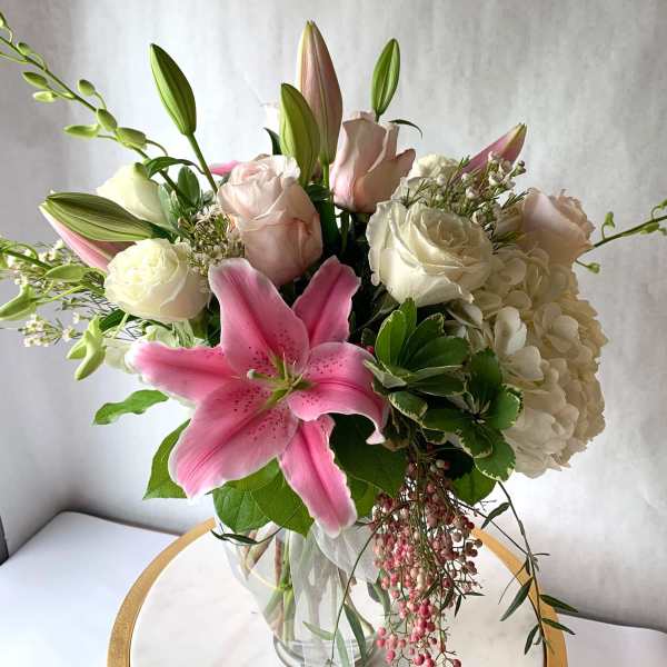 Pink lily, white hydrangea, and pale roses arranged in a clear glass vase