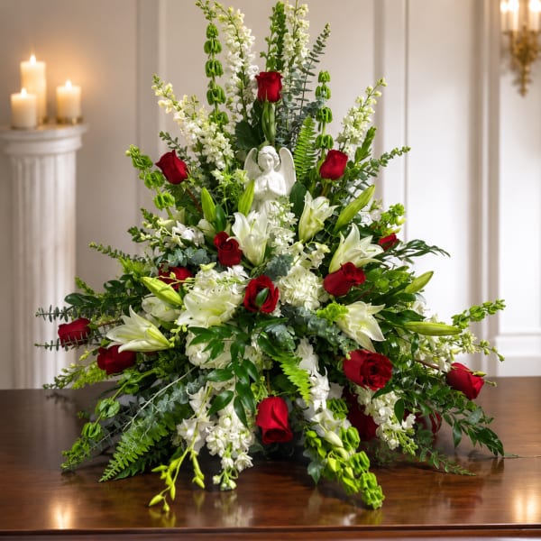 Large floral arrangement with red roses and white lilies around a small angel figurine