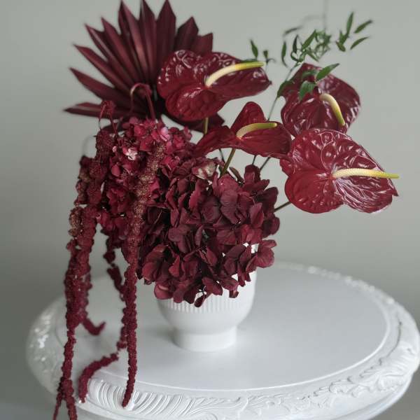 Deep burgundy floral arrangement in a white vase with hanging blooms