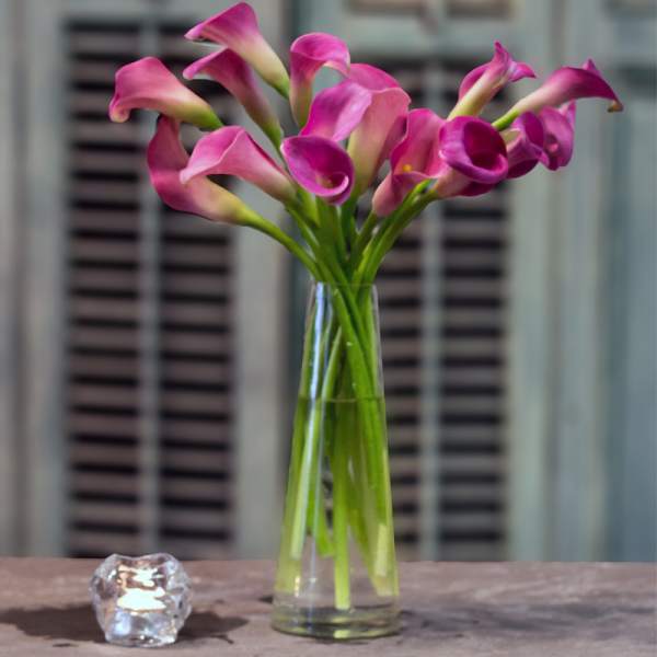Pink calla lilies in a clear glass vase beside a small candle holder