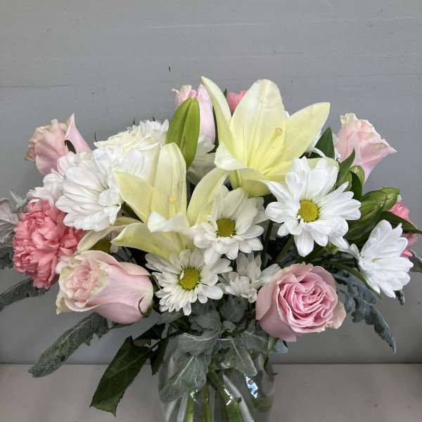 Pink roses, white daisies, and pale yellow lilies in a glass vase