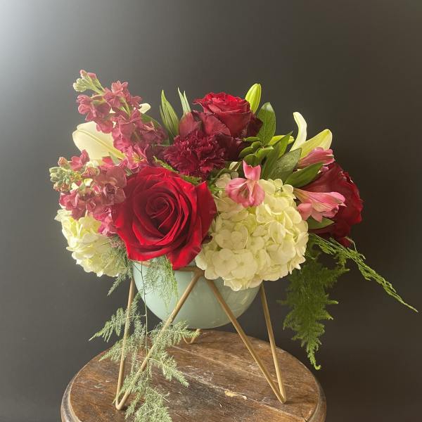 Low arrangement of red roses, white hydrangeas, and pink blooms in a mint bowl on a gold stand