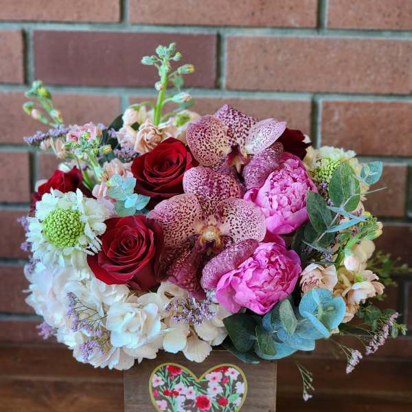 Mixed bouquet of red roses, pink blooms, and spotted orchids in a wooden box
