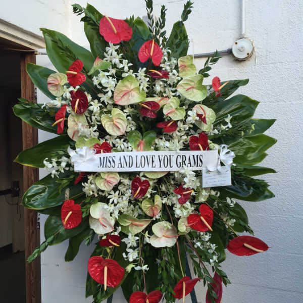 Large standing floral tribute with red and pale green blooms and a memorial ribbon