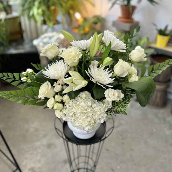 White floral arrangement in a white vase with lilies, roses, and chrysanthemums