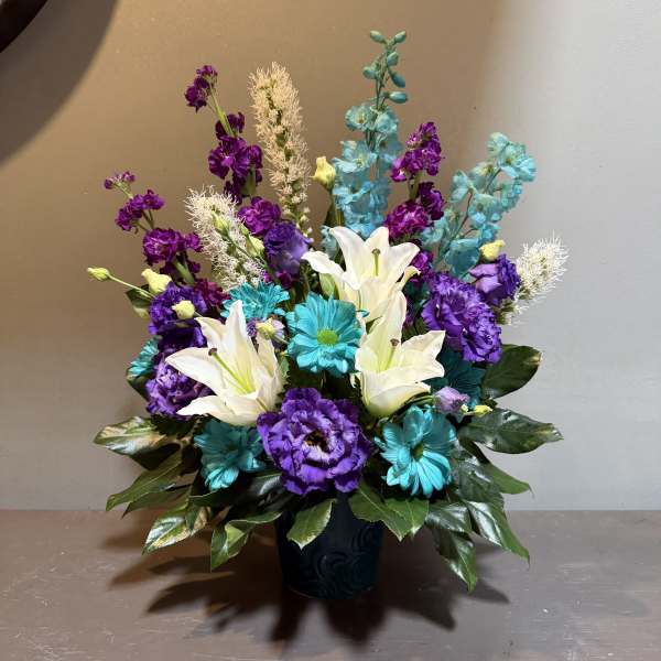 Colorful bouquet with white lilies, purple blooms, and blue flowers in a dark vase