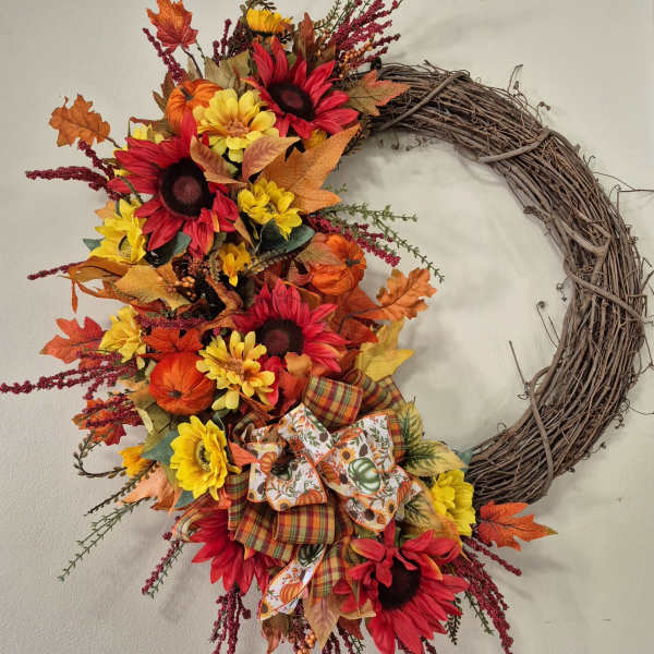 Fall wreath with sunflowers, red daisies, and ribbon on a grapevine ring