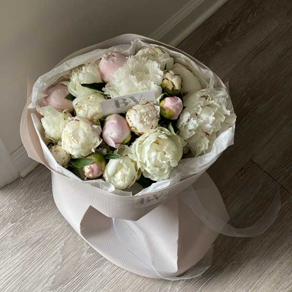Bouquet of white and pale pink peonies wrapped in blush paper