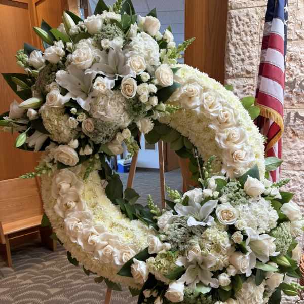 Large white floral wreath on an easel with roses and lilies