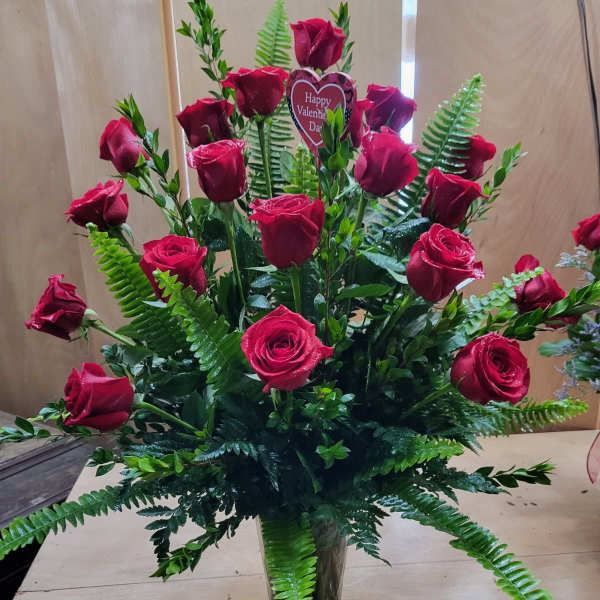 Tall bouquet of red roses in a clear glass vase with fern foliage