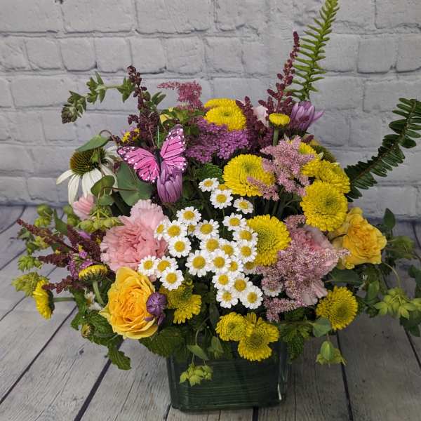 Mixed bouquet of yellow, pink, and white flowers in a square vase