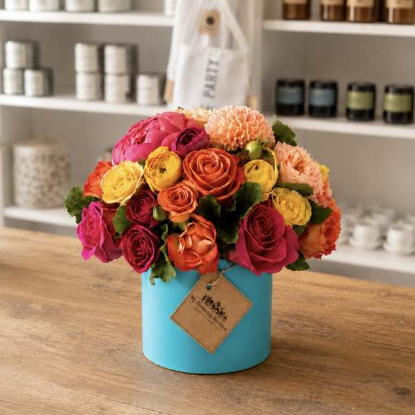 Bright mixed bouquet of roses and ranunculus in a turquoise hatbox