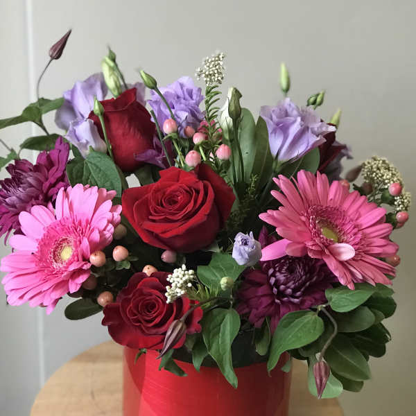 Bouquet of red roses, pink gerberas, and purple blooms in a red container