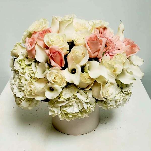 Low arrangement of white hydrangeas, cream and blush roses, and calla lilies in a round white vase