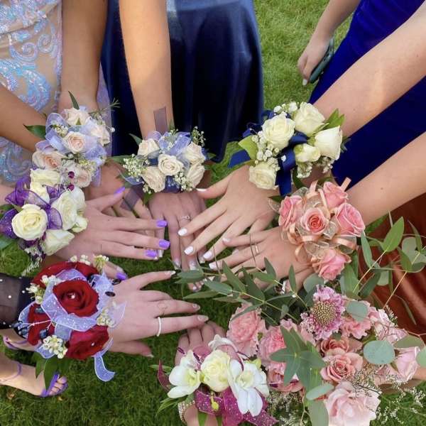 Hands holding small floral wrist corsages in assorted colors on grass