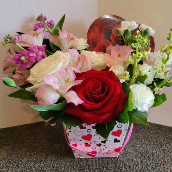 Mixed pink, white, and red flower arrangement in a heart-patterned gift bag
