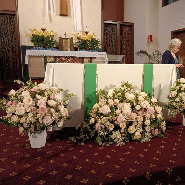 Three white floral arrangements with pale pink roses at an altar