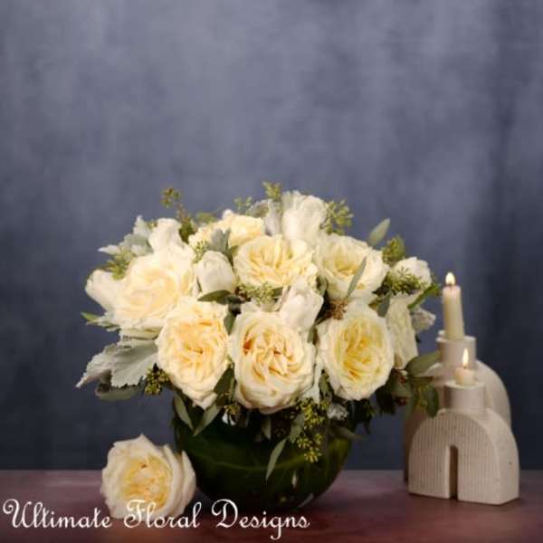 Cream roses arranged in a dark vase beside two candles
