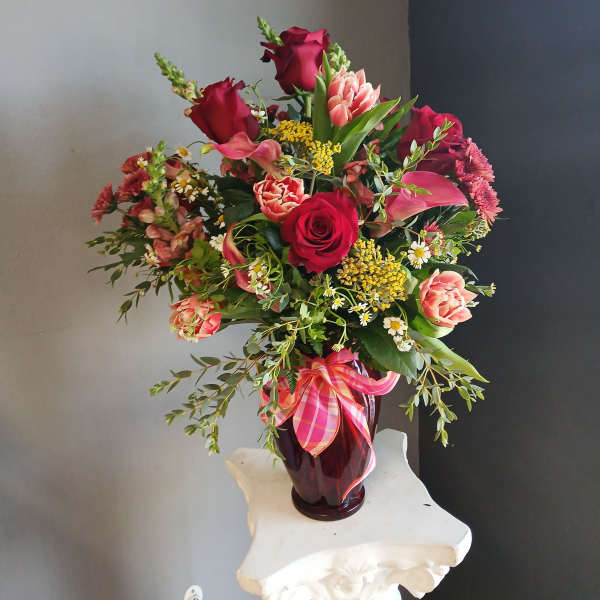 Mixed bouquet of red and pink flowers in a dark glass vase with a plaid ribbon.