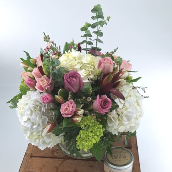 Pink roses and white hydrangeas in a glass vase with a candle beside on a wooden surface