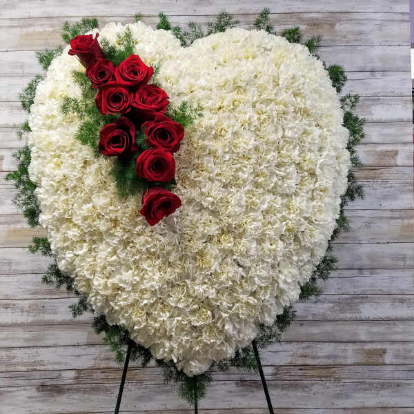 Heart-shaped white floral spray with red roses on a stand