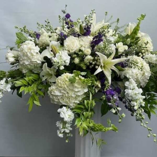 Large white floral arrangement with lilies and roses on a pedestal