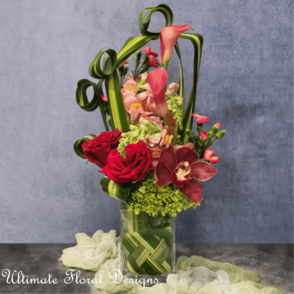 Tall floral arrangement with red roses and pink calla lilies in a glass vase