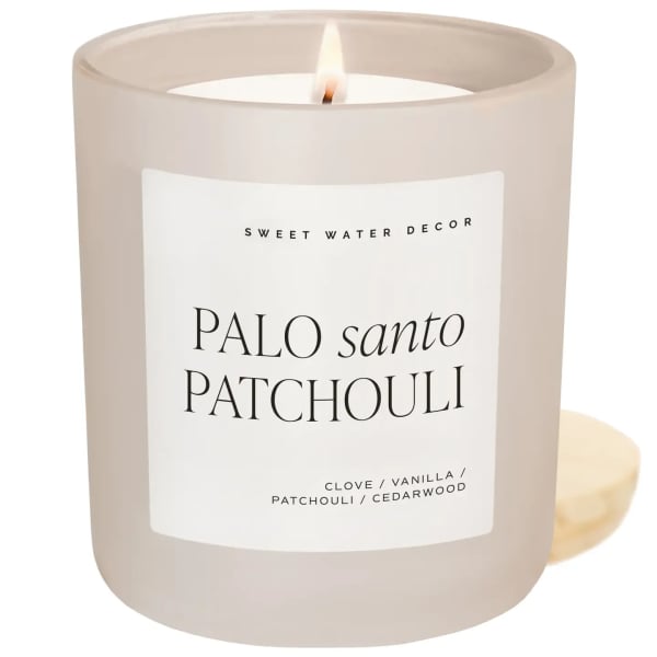 Lit beige candle in a glass jar with a white label