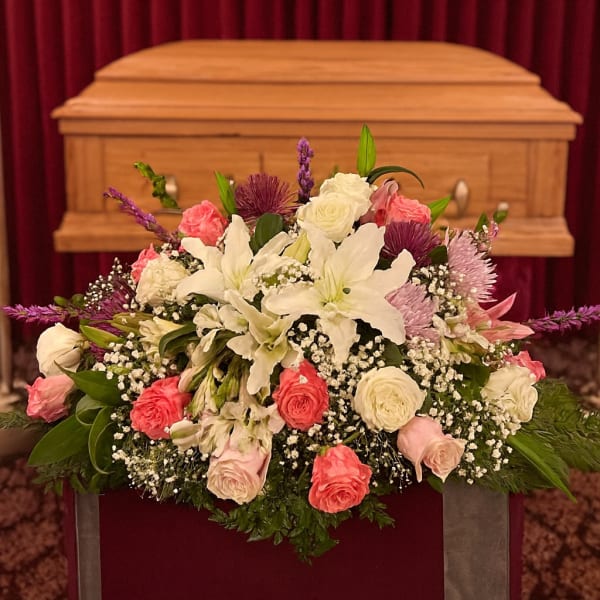 White lilies and pink roses arranged in front of a casket