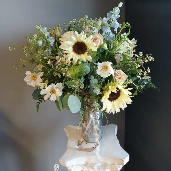 Mixed bouquet with sunflowers, white daisies, and pale roses in a glass vase