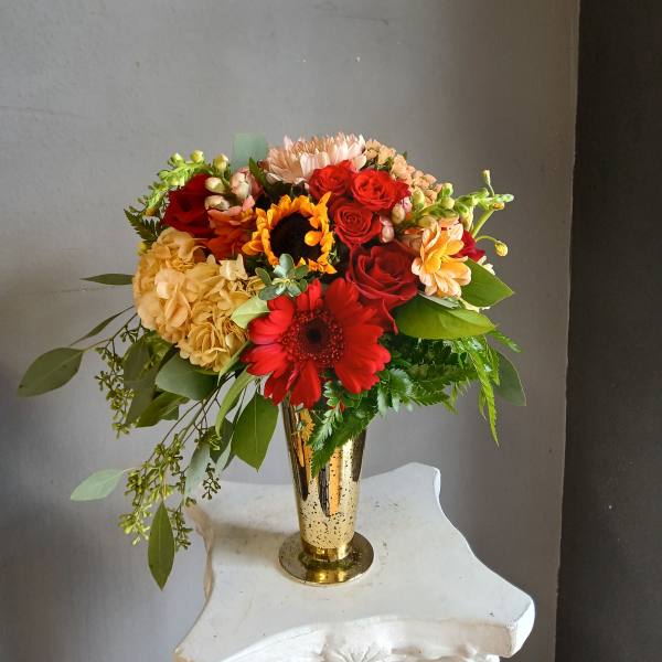 Mixed bouquet of red roses, gerbera daisies, and hydrangea in a gold vase
