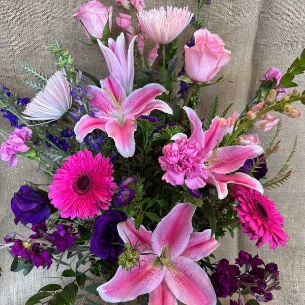Pink lilies and gerbera daisies in a glass vase with purple flowers