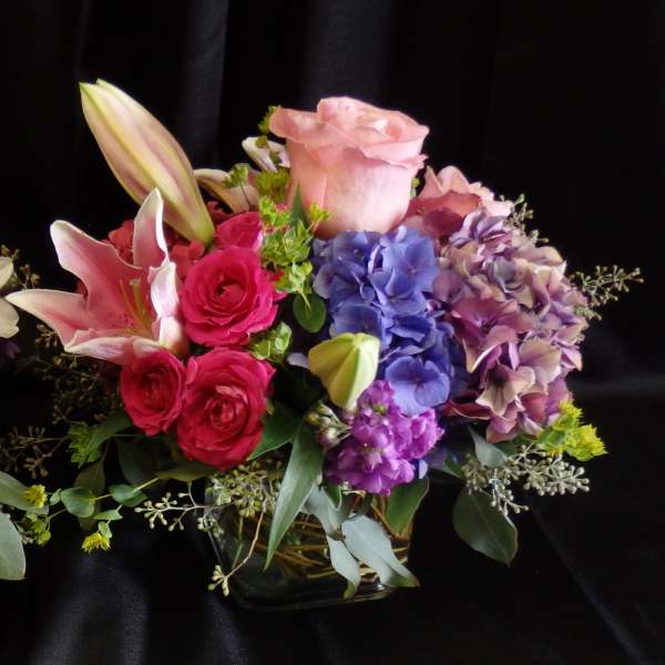Mixed bouquet of pink roses, lilies, and purple hydrangeas in a glass vase