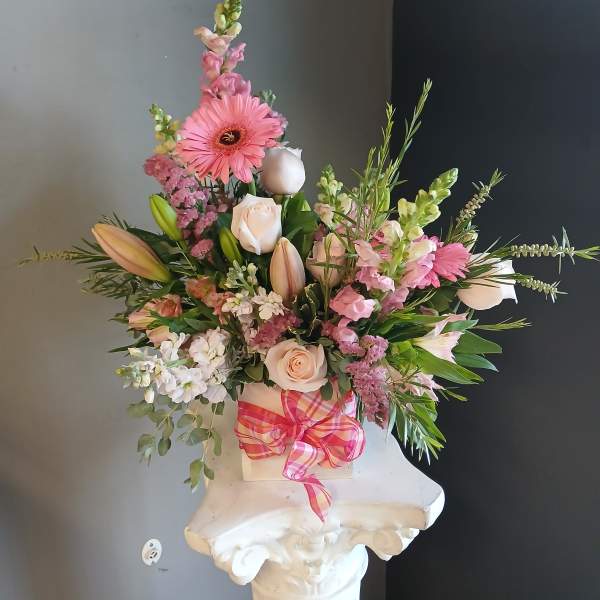 Pink and white mixed flower arrangement in a white container with a plaid ribbon