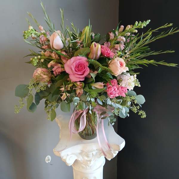 Pink and blush floral arrangement in a glass vase with a pink ribbon